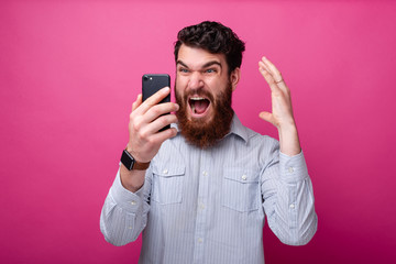 young bearded man shocked looking at his phone gesturing.