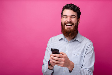 Cheerful bearded man looking at the camera and typing something on his phone.