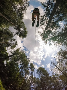 Aerial view of a person crossing the forest through a large zip line cable.