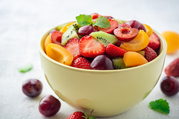 Healthy fresh fruit salad in bowl on gray concrete background. Selective focus.