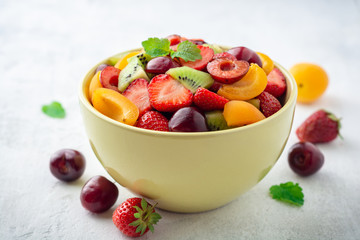 Healthy fresh fruit salad in bowl on gray concrete background. Selective focus.