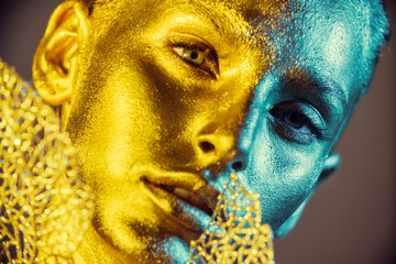 Fashion model woman golden skin face in bright sparkles, Trendy glowing gold skin make-up. Glitter metallic shine makeup 