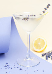 Cold, refreshing lavender lemonade, martini on a bright yellow-lilac background with ice, lemon and lavender flowers on the background with space for text.