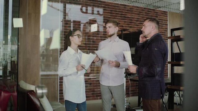 group of young businesspeople standing together in a modern office watching their manager draw a graph on a glass   wall