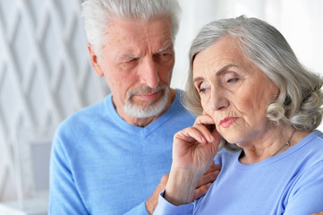 Sad beautiful senior couple posing at home