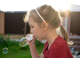 A little girl blowing soap bubbles in summer park.