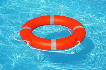 Orange lifebuoy pool ring float on blue water. Life ring floating on top of sunny blue water. Life ring in swimming pool