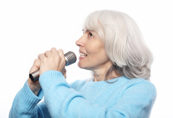 lifestyle, emotion and people concept: Happy old senior woman singing with microphone, having fun, expressing musical talent over white background