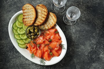 Appetizer - salted salmon, pieces of cucumber, capers, dill and grilled bread. Top view, 