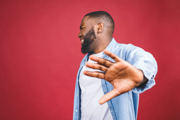 Portrait of African American male holding hand in stop sign, warning and preventing you from something bad, looking at the camera with worried expression. Selective focus on the palm