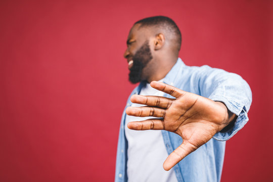 Portrait of African American male holding hand in stop sign, warning and preventing you from something bad, looking at the camera with worried expression. Selective focus on the palm