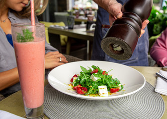 Concept restaurants, guest service. The waiter fills the salad with fresh pepper.
