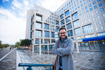 Happy male businessman standing in a front of building