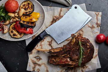 Tomahawk steak with vegetables and a knife on the table. Grilled meat with grilled vegetables and...