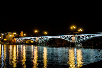 Fototapeta na wymiar Triana Bridge in Seville at night with its lights reflected in the Guadalquivir River