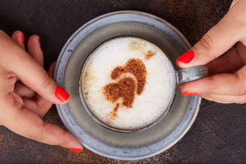 Woman holding a cup of cappuccino coffee with cinnamon hearts on the top