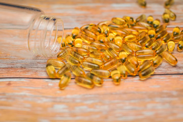 Close up nutritional supplement gold capsules spilled out of clear bottle on wooden table in selective focus.