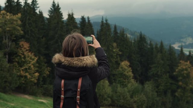 Young girl hiker is shooting video of beautiful misty mountain landscape on mobile phone camera. Lifestyle adventure. Back view, toning, 4k, Editorial video