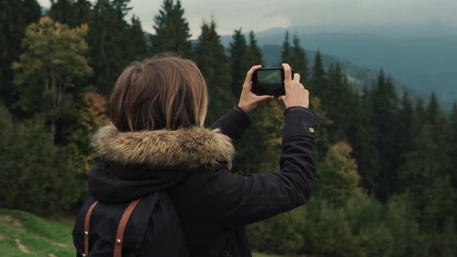 Young girl hiker is shooting video of beautiful misty mountain landscape on mobile phone camera. Lifestyle adventure. Back view, toning, 4k, Editorial video