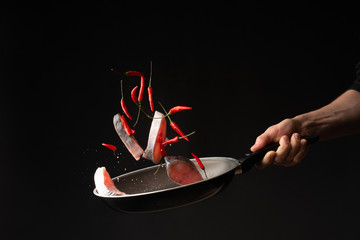 Closeup. Chef cook roasting fish with small red hot pepper on a griddle against a black background....