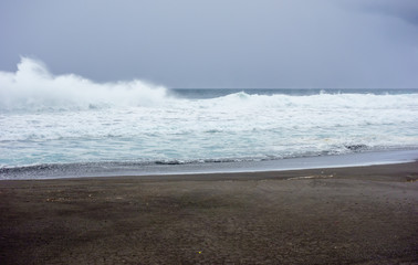 Ocean waves crashing on wet beach under dark clouds.