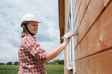 a young woman paints the outside wall of a new wooden house. the process of painting a country house