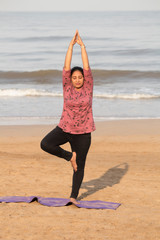 Fototapeta na wymiar Woman in yoga Vrikshasana tree pose at beach