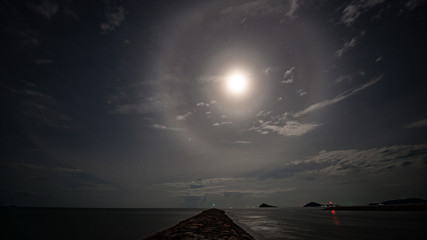 stunning beautiful big lunar ring and bright moon in little cloudy sky night floating over seascape...