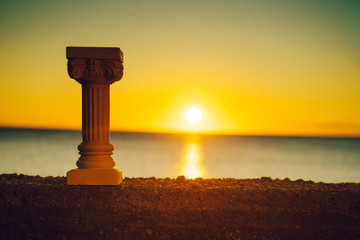 Greek column on shore and sunset over sea surface