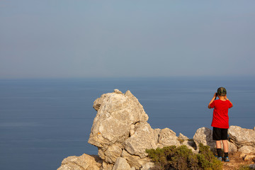 Fototapeta premium Little boy looking at binoculars on blue sea in Rhodes Greece. The child is on a high mountain.
