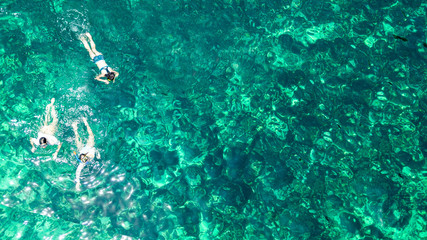 Naklejka na ściany i meble Aerial top view of family snorkeling from above, mother and kids snorkelers swimming in a clear tropical sea water with corals during summer vacation in Thailand