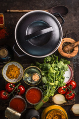 Cast iron pot with fresh ingredients for tasty vegetarian tomato soup or sauce cooking: tomatoes, herbs, spices, canned tinned tomatoes. Top view. Healthy eating. Homemade cooking. Rustic style