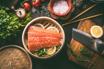 Salmon fillet and lemon slices in bamboo steamer on dark rustic kitchen table with ingredients and tools. Healthy eating and cooking. Asian cuisine - obrazy, fototapety, plakaty