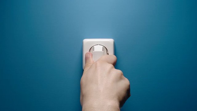 Man Inserts Plug Into Electrical Socket On A Blue Wall