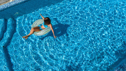 Aerial view of beautiful girl in swimming pool from above, swim on inflatable ring donut and has fun in water on family vacation on tropical holiday resort