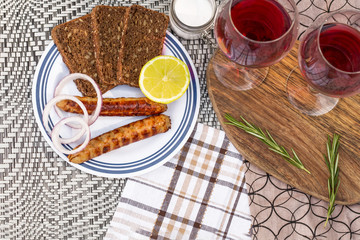 Picnic, barbecue in nature. Red wine, grilled sausages, vegetables and bread on a beautiful tablecloth.