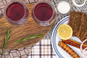 Picnic, barbecue in nature. Red wine, grilled sausages, vegetables and bread on a beautiful tablecloth.