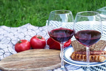 Two glasses of elite red wine. In the background are sausages grilled, vegetables, bread.