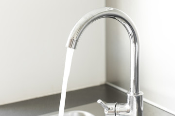 Mixer tap with water flowing. Chrome faucet and washbasin