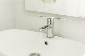 Mixer tap with water flowing. Chrome faucet and washbasin
