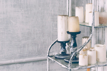 Candles with vintage stand on shelf, gray wall background, toned. Close-up, copy space
