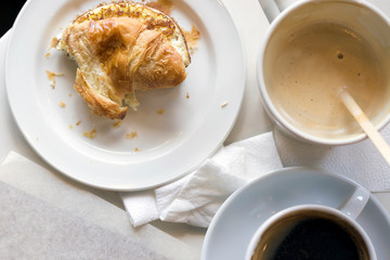 Not finished breakfast with croissant and coffee soft focus on the table, sunlight, toned. Top view, close up, copy space
