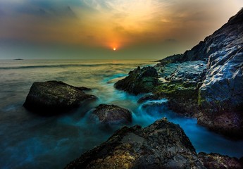sunset or golden hours by the sea side or beach, a long exposure shot, water touching the rocks in...