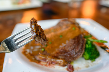Fork dipping grilled rib eye beefsteak sliced