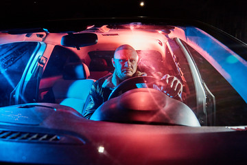 Fototapeta premium Male driver in a leather jacket in the car in the dark. Night photo shoot