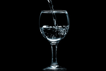 Pour water into glass on black background.