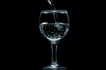 Pour water into glass on black background.