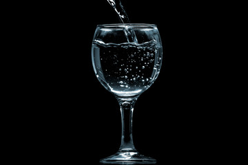 Pour water into glass on black background.