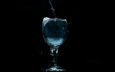 Pour water into glass on black background.