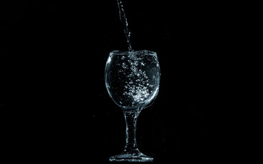 Pour water into glass on black background.